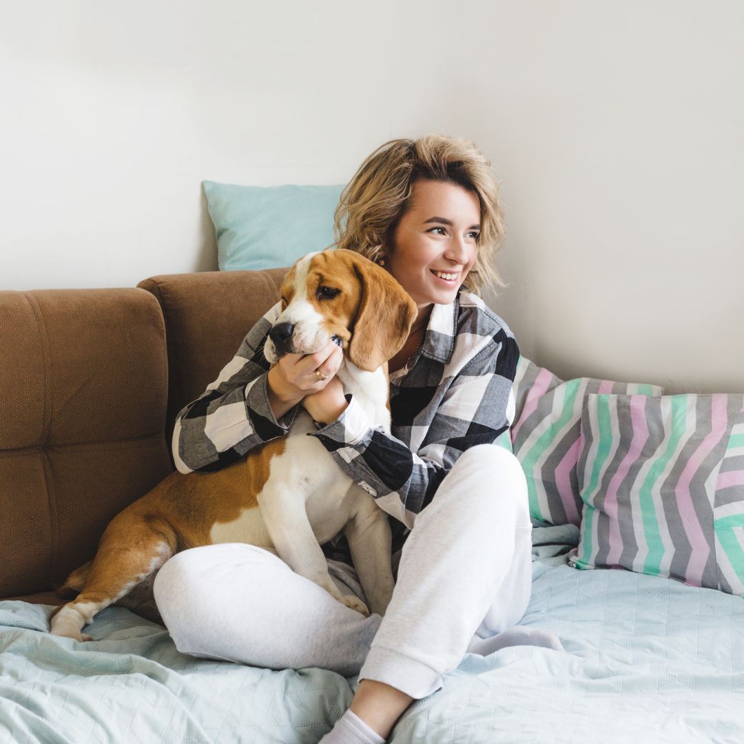 Person smiling will cuddling with their dog on a bed