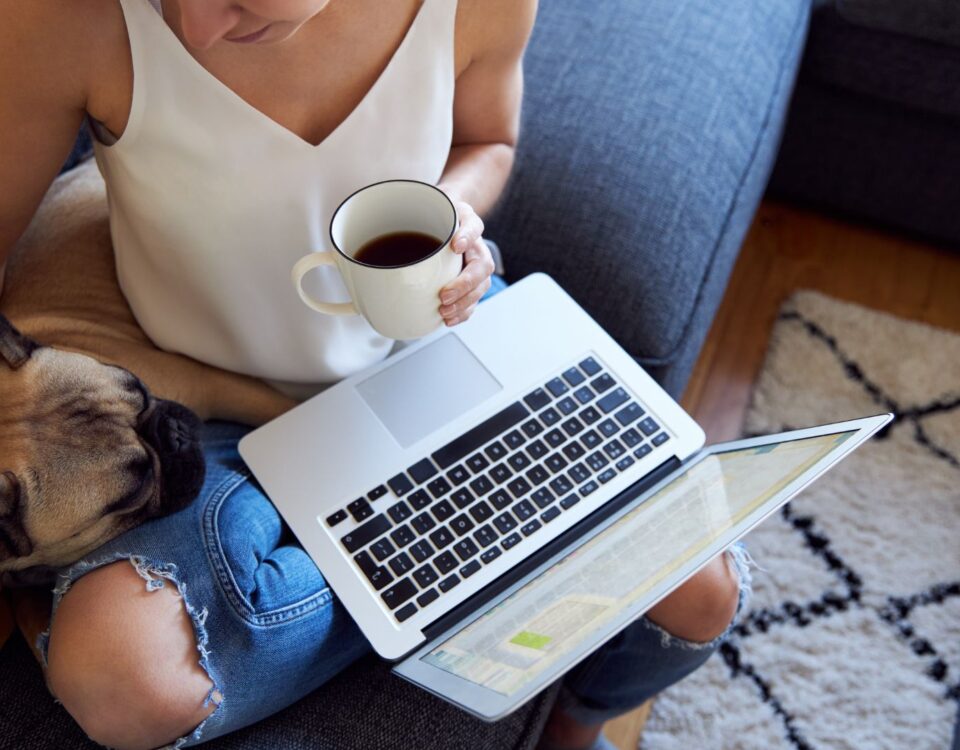 Person using a laptop while sitting by their dog